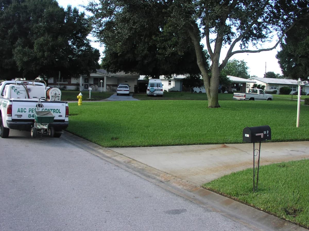 Two ABC Pest Control branded trucks parked on a lush green lawn with company sign